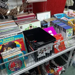 Uitgestalde tweedehands spullen op tafels: vinyl records, boeken, dvd's, speelgoed en kleding in bakken