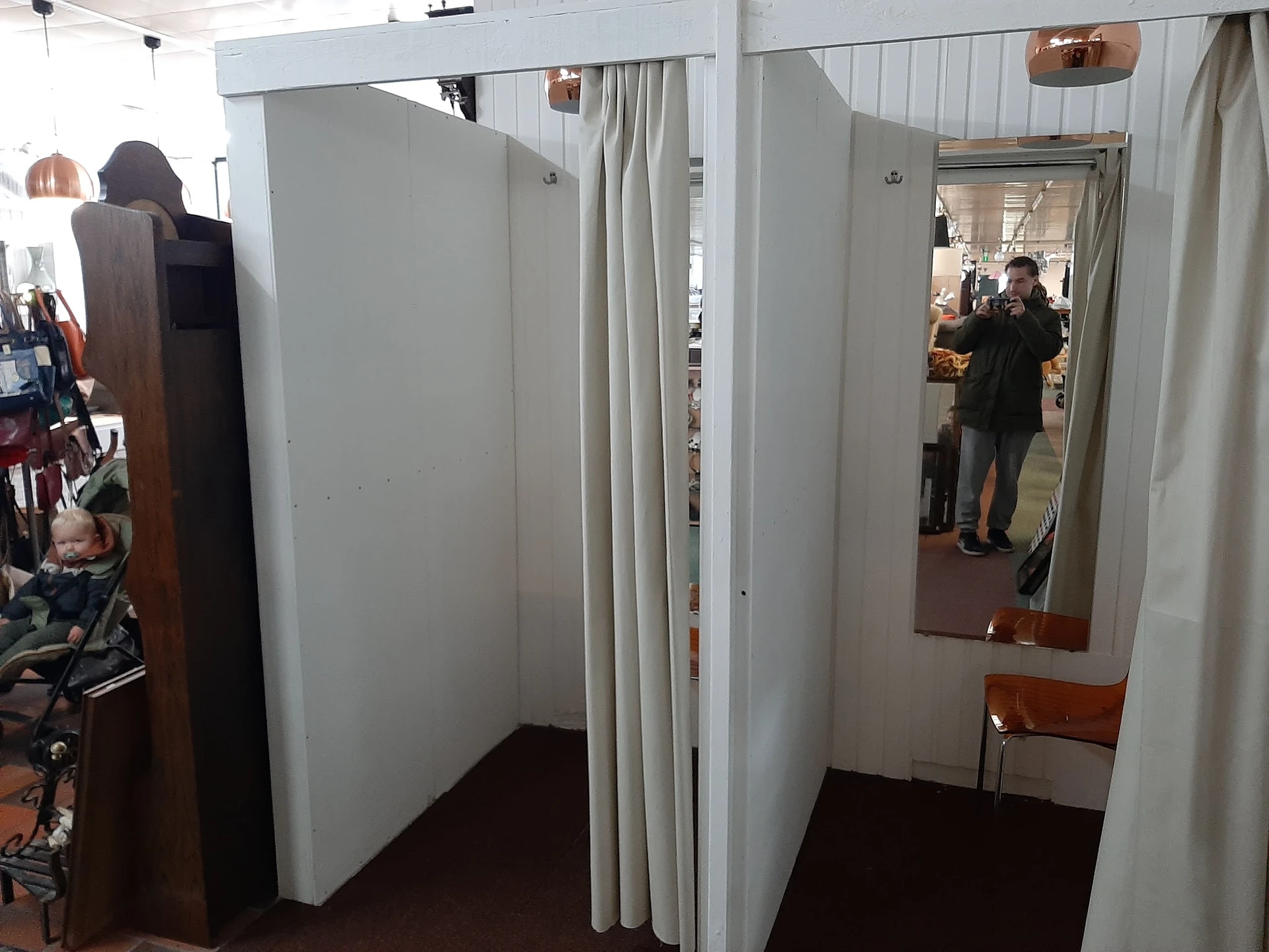 Witte paskamers met gordijnen en spiegels in kringloopwinkel, mensen zichtbaar op achtergrond