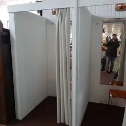 Witte paskamers met gordijnen en spiegels in kringloopwinkel, mensen zichtbaar op achtergrond