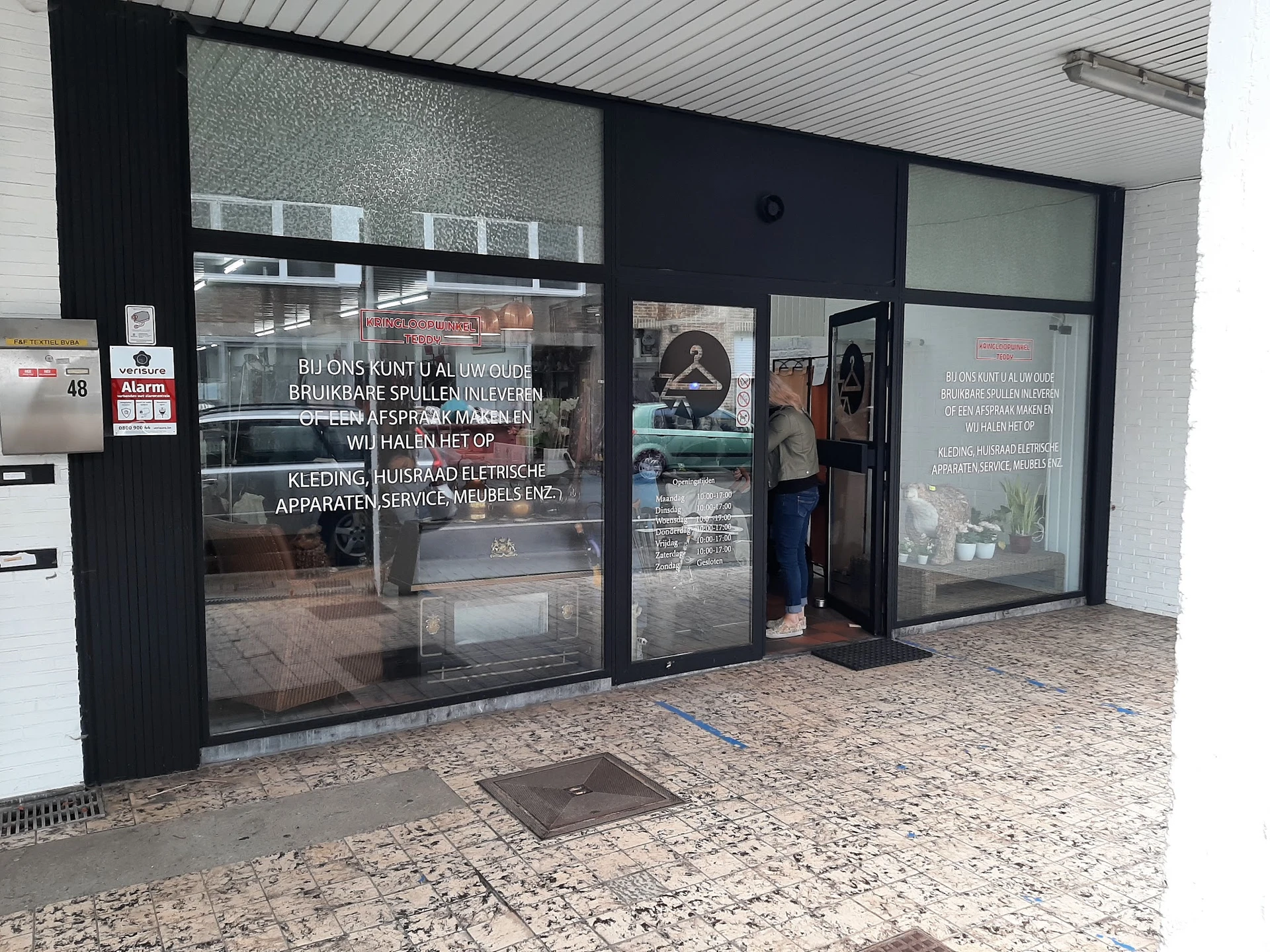 Winkelgevel met grote glazen deuren en ramen, zwarte frames, witte plafond, uitgestalde spullen zichtbaar achter glas