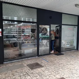 Winkelgevel met grote glazen deuren en ramen, zwarte frames, witte plafond, uitgestalde spullen zichtbaar achter glas