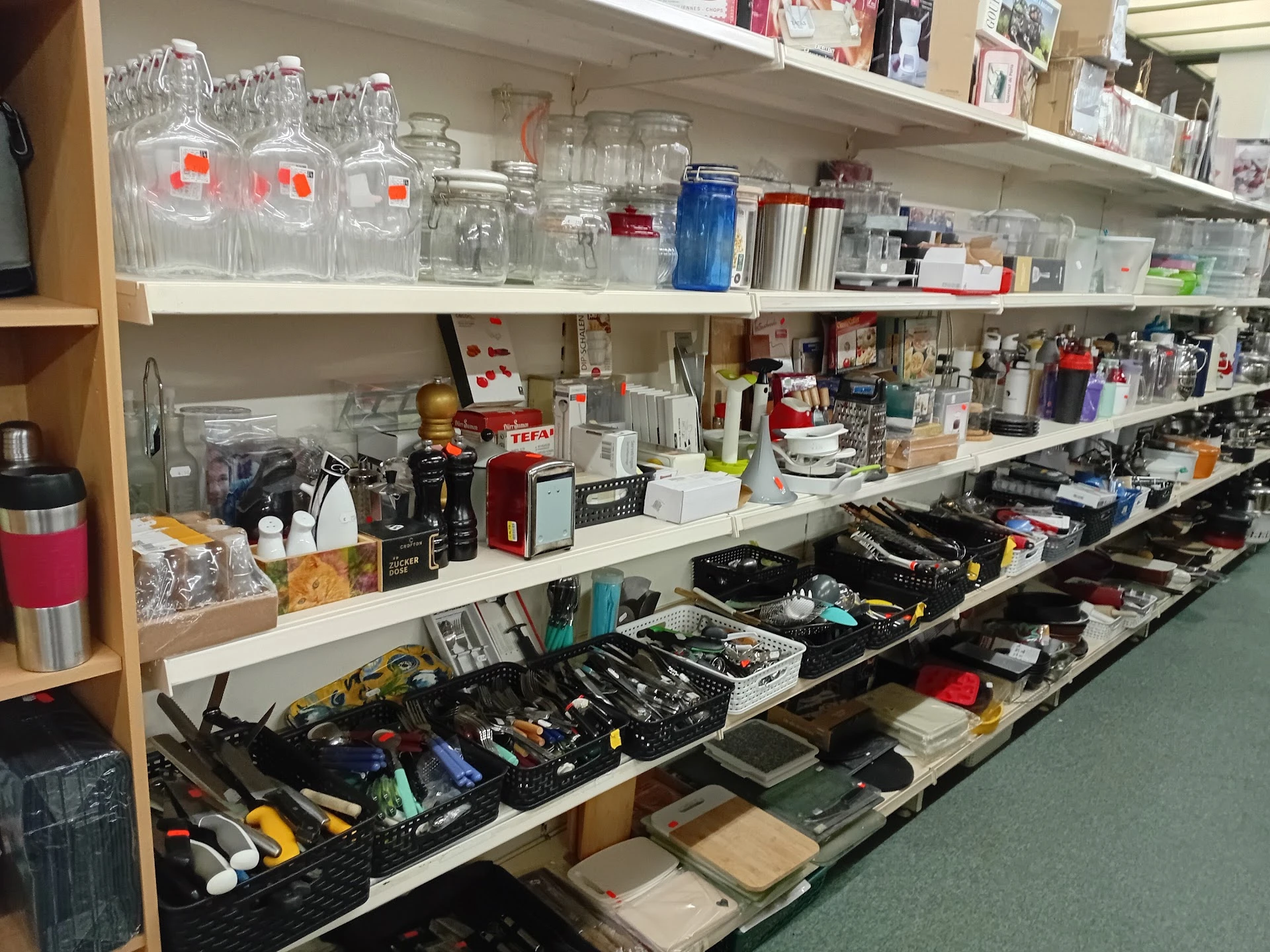 Schappen met glazen potten, huishoudartikelen en gereedschap in een kringloopwinkel