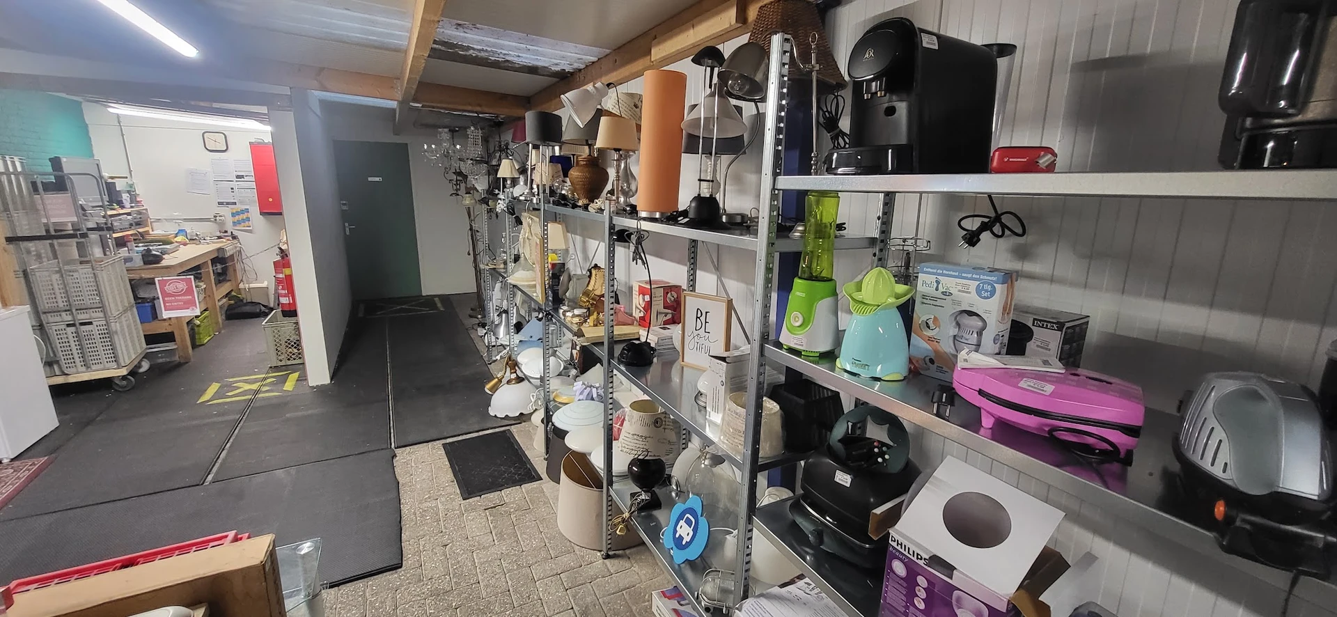 Winkelvloer met stellingen vol huishoudapparatuur, keukengerei en kleine electronica in een kringloopwinkel