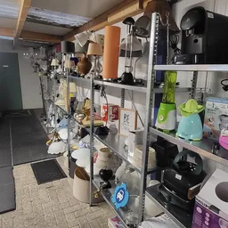 Winkelvloer met stellingen vol huishoudapparatuur, keukengerei en kleine electronica in een kringloopwinkel