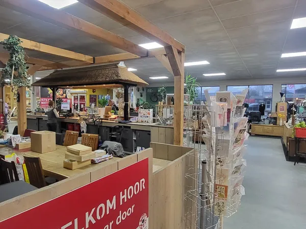 Binnenaanzicht van kringloopwinkel met houten balkenstructuur, toonbank met rode zijde, diverse displays en stellingen met sp