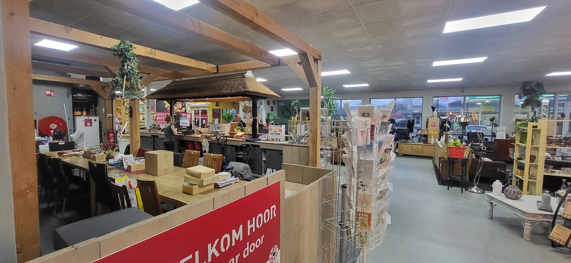 Binnenaanzicht van kringloopwinkel met houten balkenstructuur, toonbank met rode zijde, diverse displays en stellingen met sp