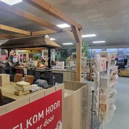 Binnenaanzicht van kringloopwinkel met houten balkenstructuur, toonbank met rode zijde, diverse displays en stellingen met sp