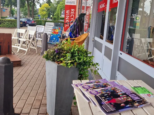 Winkelterras met witte stoelen, bloembakken en uitgestalde spullen voor de winkelingang