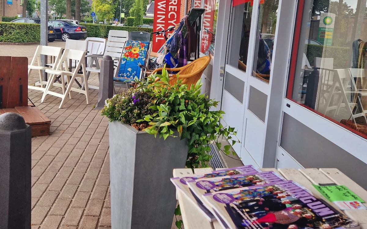 Winkelterras met witte stoelen, bloembakken en uitgestalde spullen voor de winkelingang