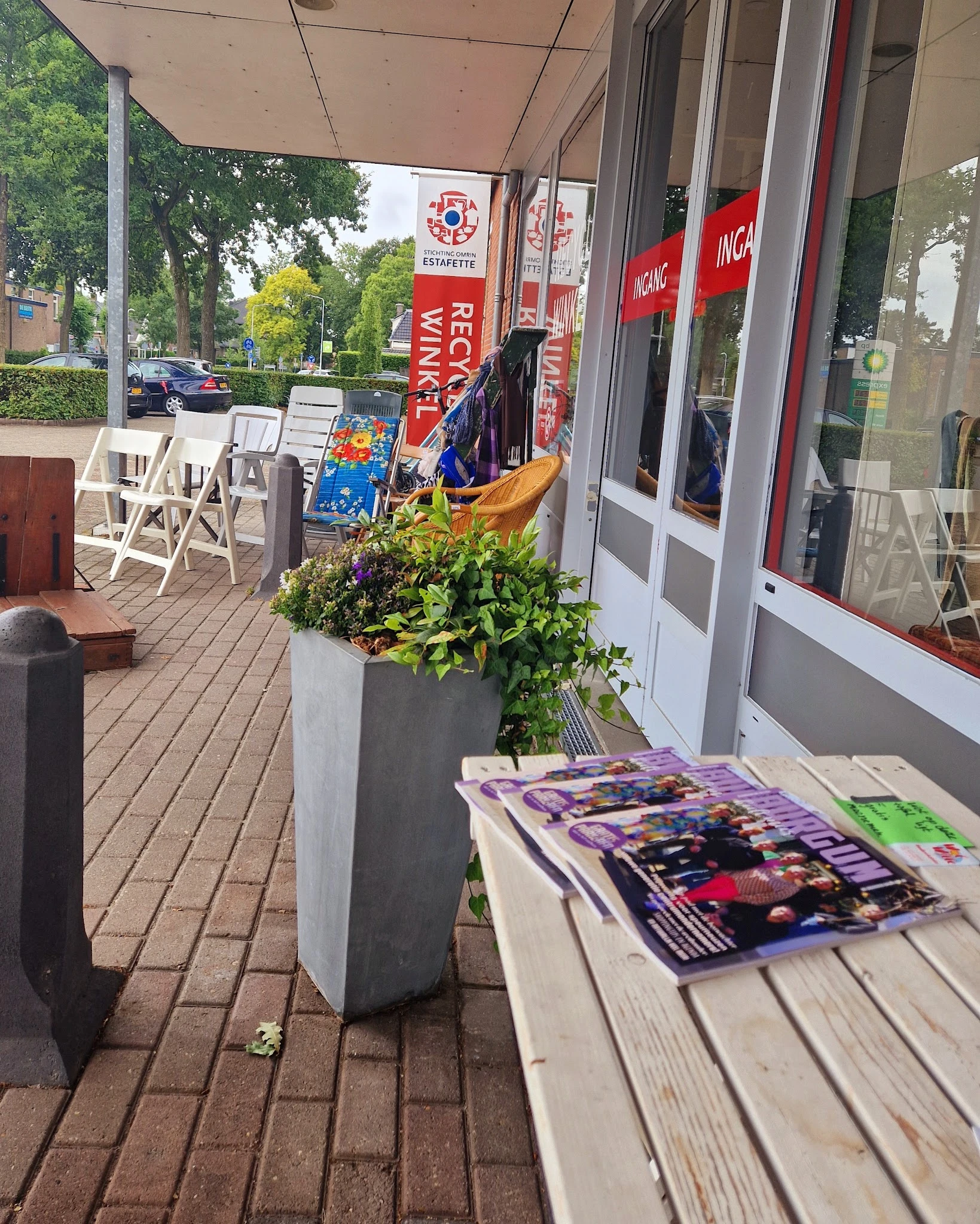 Winkelterras met witte stoelen, bloembakken en uitgestalde spullen voor de winkelingang