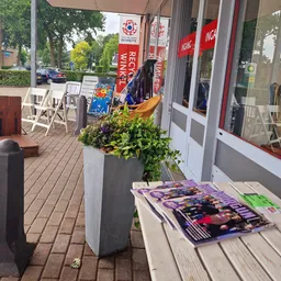 Winkelterras met witte stoelen, bloembakken en uitgestalde spullen voor de winkelingang