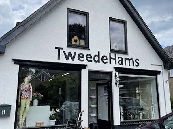 Witte gevel van tweedehandswinkel met zwart kozijn, grote etalageruiten en winkelnaam op voorgevel