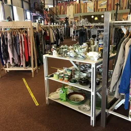 Kringloopwinkel met kledingrekken en een centrale toonbank met huishoudelijke spullen