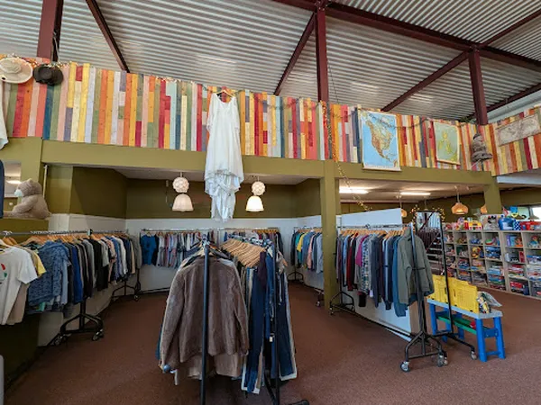 Winkelinterieur met kledingrekken, boekenkast aan muur en bruine vloer
