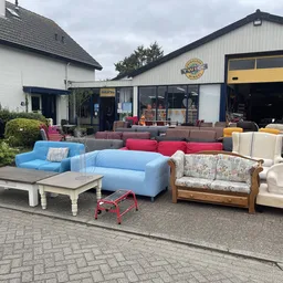 Uitgestalde meubels op het terras: blauwe fauteuils, rode zitbank, houten bankje en crèmekleurige stoelen