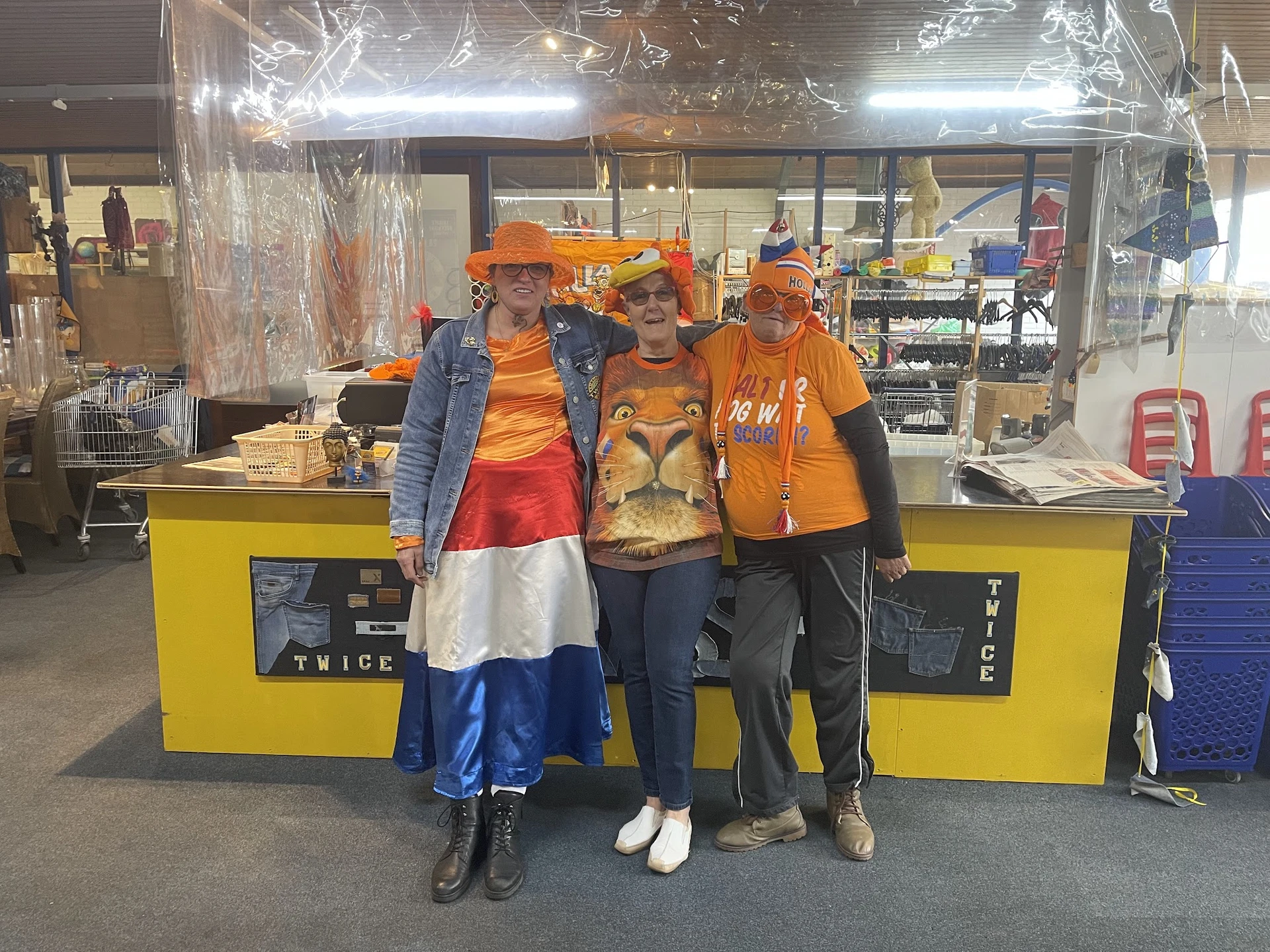 Vier mensen in oranje kleding en oranje petten poseren voor de gele balie van de winkel