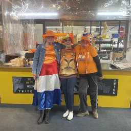 Vier mensen in oranje kleding en oranje petten poseren voor de gele balie van de winkel