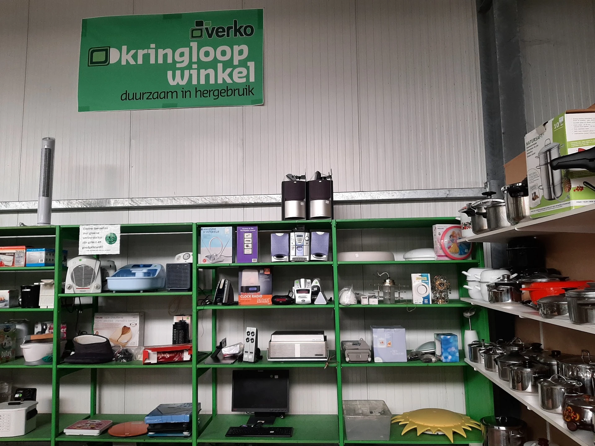 Groene stellingen met diverse tweedehands spullen en huishoudartikelen in een kringloopwinkel