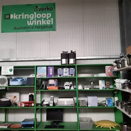 Groene stellingen met diverse tweedehands spullen en huishoudartikelen in een kringloopwinkel