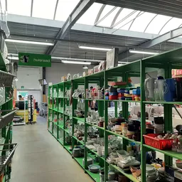 Winkelvloer met groene stellingen vol tweedehands huishoudartikelen, kleding en diverse goederen in een kringloopwinkel
