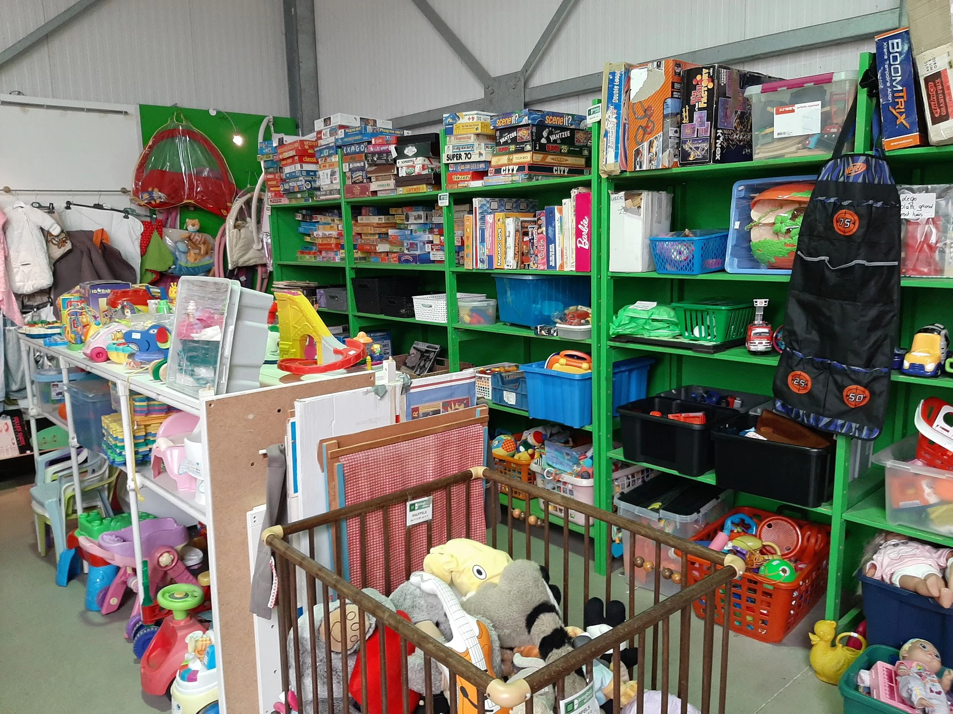 Binnenaanzicht van kringloopwinkel met groene stellingen vol speelgoed, boeken en huishoudartikelen, inclusief een babybox me