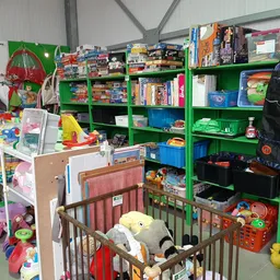 Binnenaanzicht van kringloopwinkel met groene stellingen vol speelgoed, boeken en huishoudartikelen, inclusief een babybox me