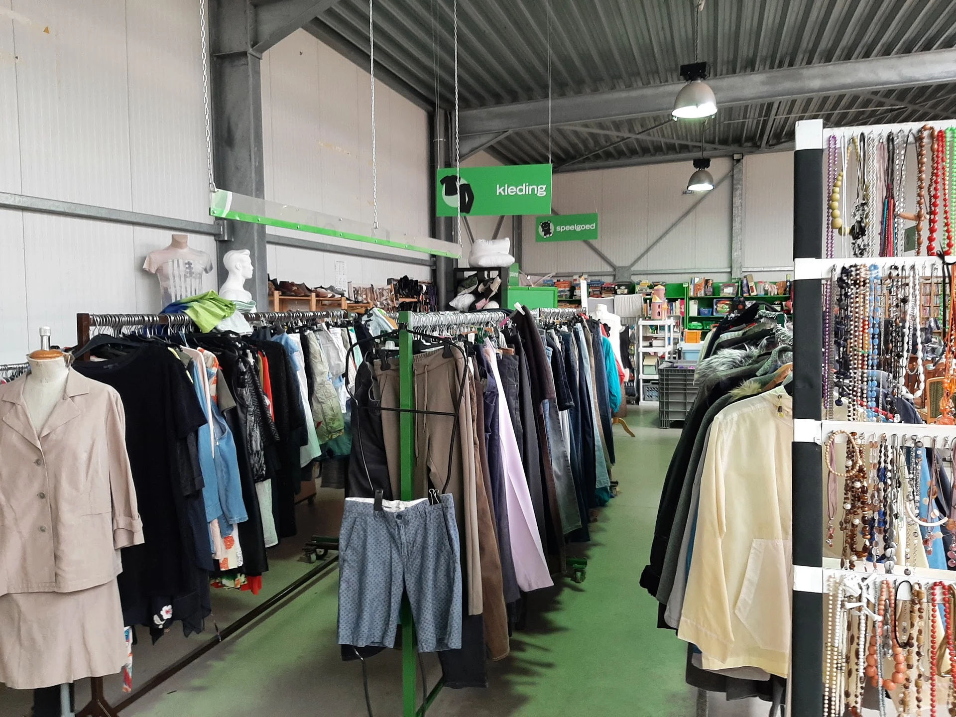 Binnenzicht van kringloopwinkel met groene vloer, rekken vol kleding en accessoires aan de wanden