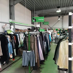 Binnenzicht van kringloopwinkel met groene vloer, rekken vol kleding en accessoires aan de wanden