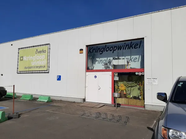Witte gevel van kringloopwinkel met rode ingang en gele uithangbord