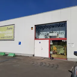 Witte gevel van kringloopwinkel met rode ingang en gele uithangbord