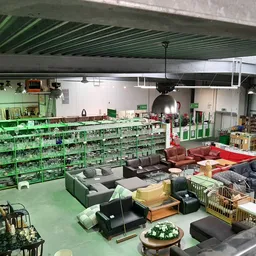 Overzicht van kringloopwinkelruimte met groene stellingen vol spullen, zitmeubels op de vloer en lichte productverlichting