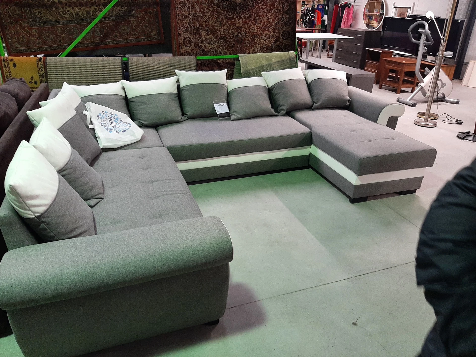 Grijze en groene hoekbank met veel kussens in een kringloopwinkel