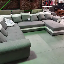 Grijze en groene hoekbank met veel kussens in een kringloopwinkel