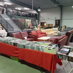 Overzicht van winkelinterieur met rode banken, boekenrek, stellingen met gebruikt huisraad en meubilair op achtergrond