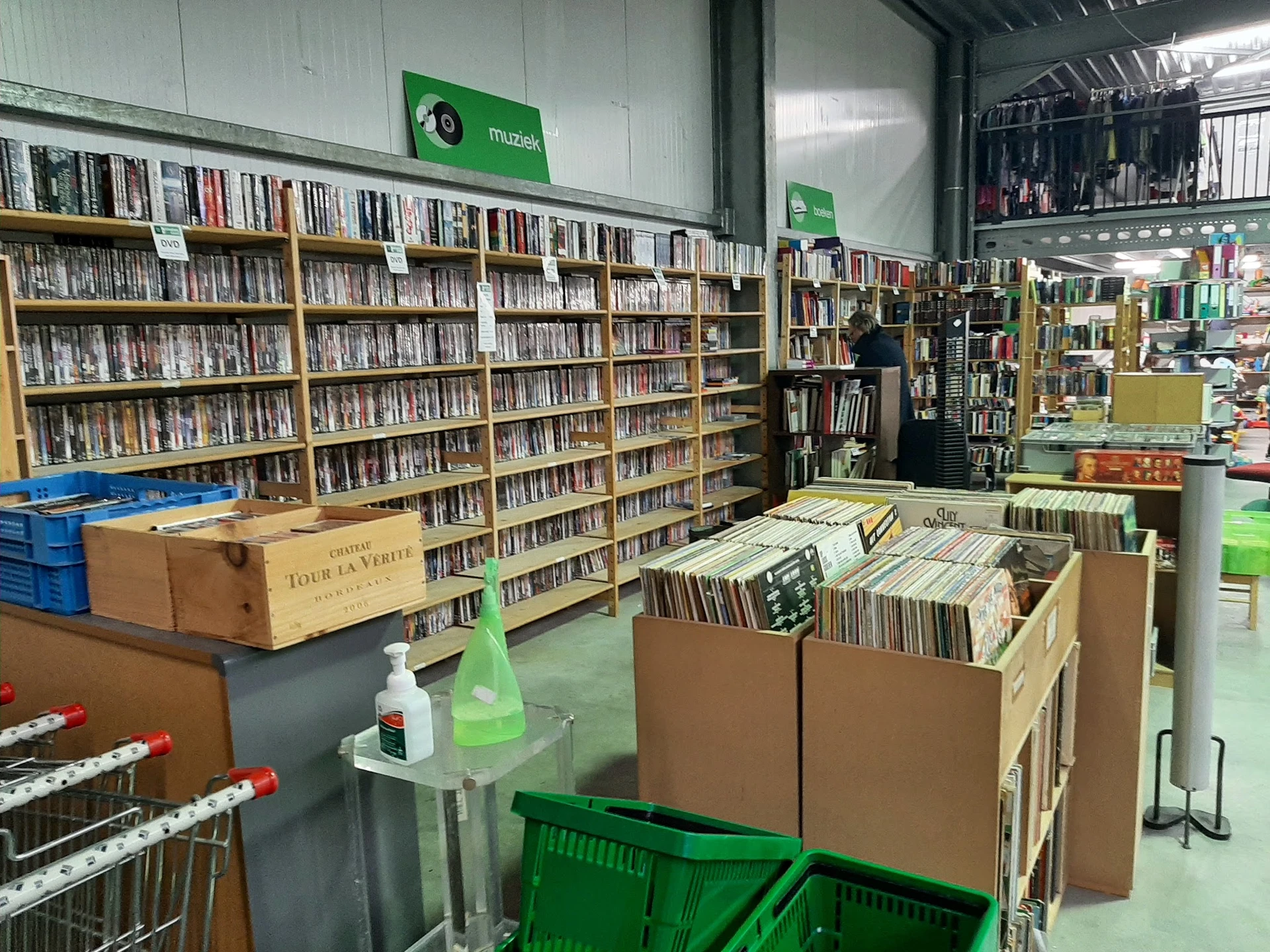 Winkelvloer met cd- en dvd-rekken, boekenkasten en kartonnen dozen met media in een kringloopwinkel