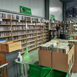 Winkelvloer met cd- en dvd-rekken, boekenkasten en kartonnen dozen met media in een kringloopwinkel