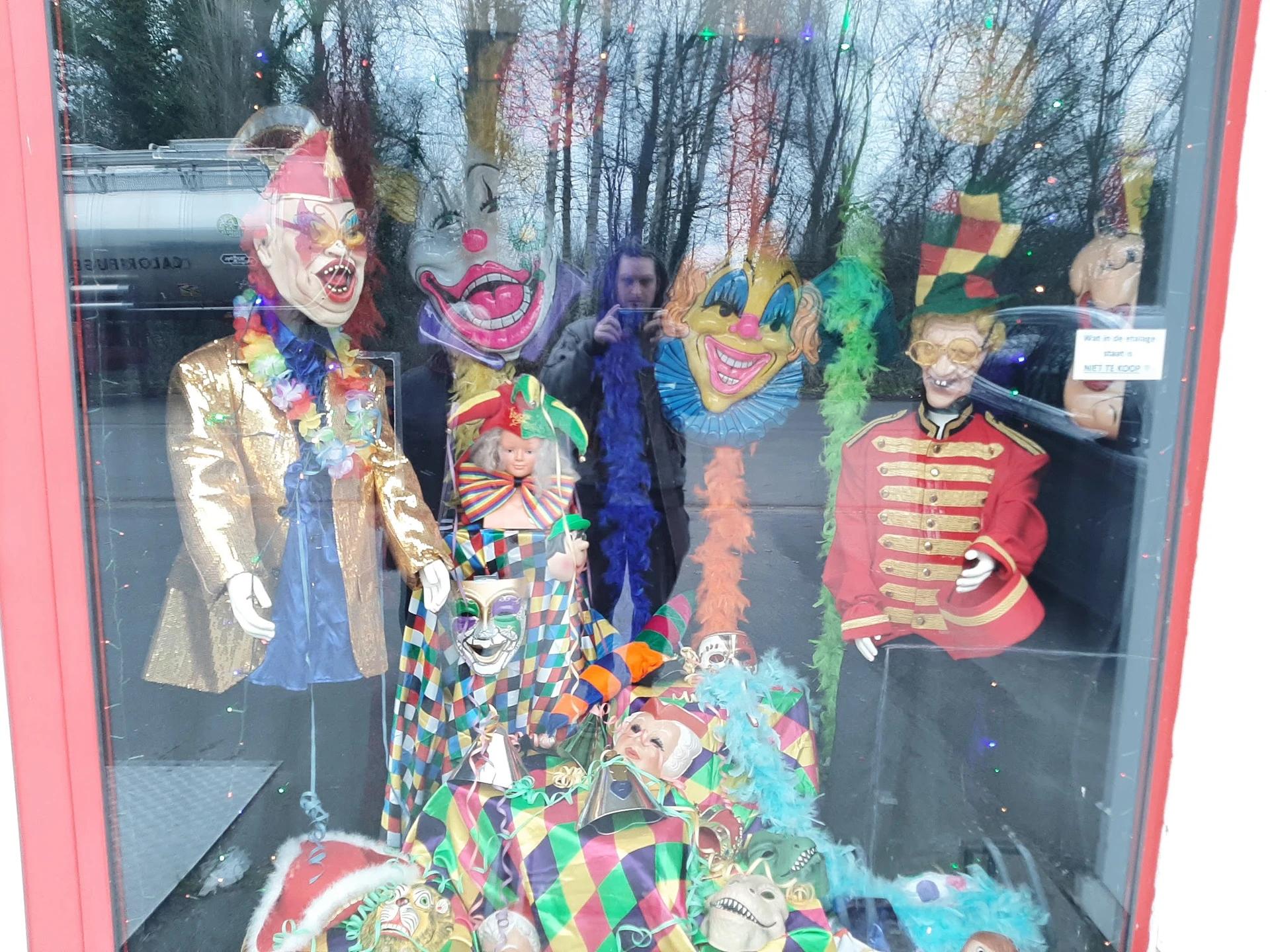 Etalage met carnavalskostuums en maskers in felle kleuren, waaronder jasjes, jurken en accessoires op mannequins