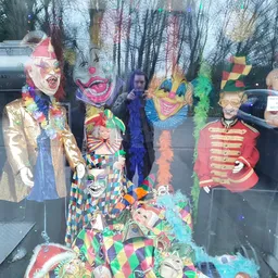 Etalage met carnavalskostuums en maskers in felle kleuren, waaronder jasjes, jurken en accessoires op mannequins