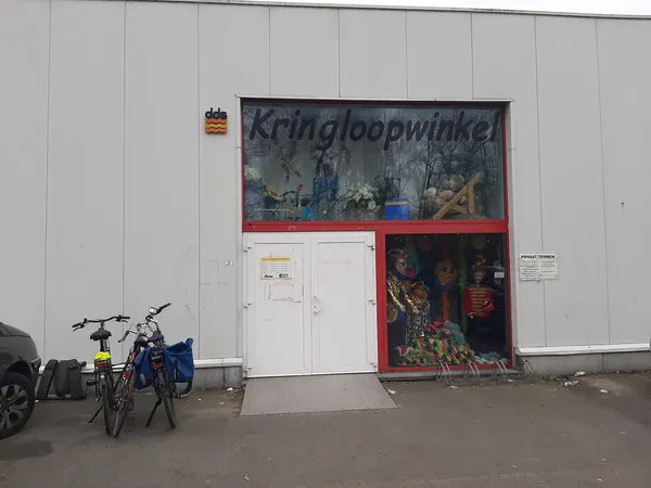 Gevel van kringloopwinkel met wit vlak en rode ingang, fietsen ervoor geparkeerd