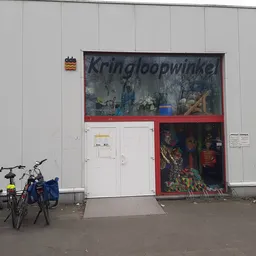 Gevel van kringloopwinkel met wit vlak en rode ingang, fietsen ervoor geparkeerd