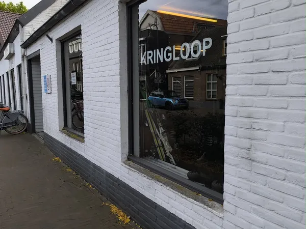 Witte bakstenen gevel van kringloopwinkel met donker raampartij en KRINGLOOP-bord