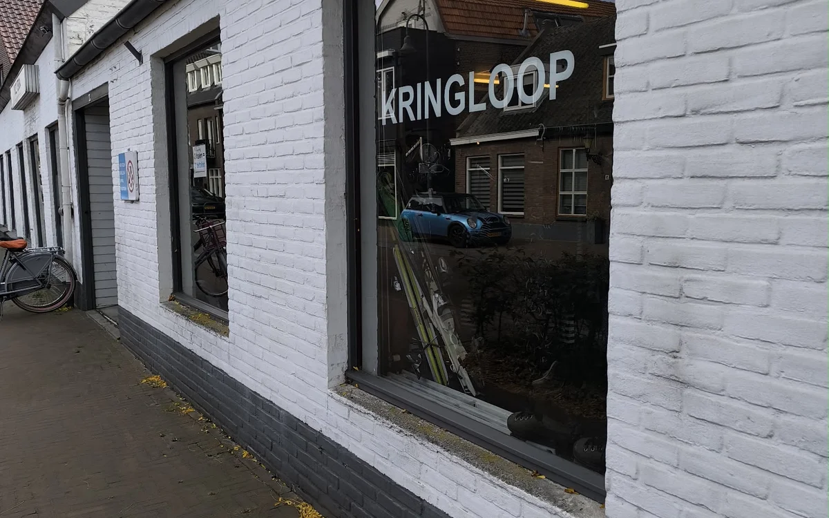 Witte bakstenen gevel van kringloopwinkel met donker raampartij en KRINGLOOP-bord