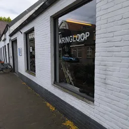 Witte bakstenen gevel van kringloopwinkel met donker raampartij en KRINGLOOP-bord