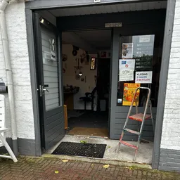 Ingang van kringloopwinkel met open deur, ladder en diversen spullen in de deuropening
