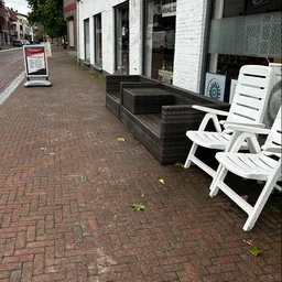 Terras met witte kunststof stoelen voor winkelpui van kringloopwinkel