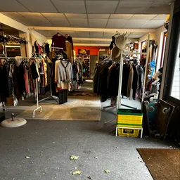 Winkelinterieur met rekken vol tweedehands kleding, gele plastic kisten en verlichte plafondlampen