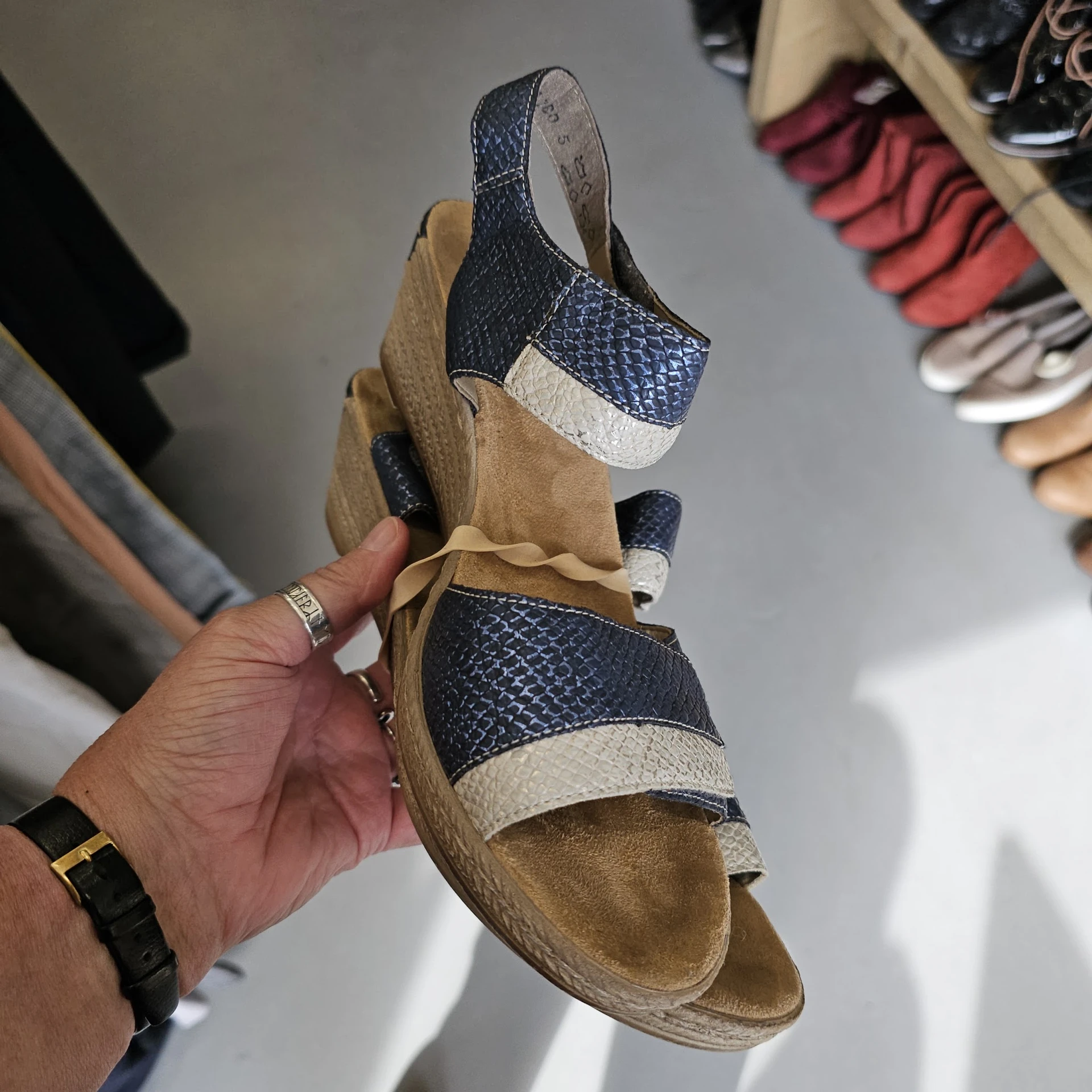Close-up van een tweedehands sandaal in beige en donkerblauw met witte accenten, gehouden in een hand