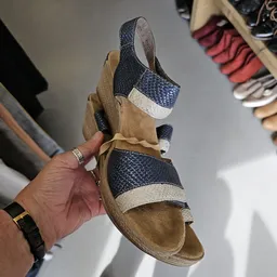 Close-up van een tweedehands sandaal in beige en donkerblauw met witte accenten, gehouden in een hand