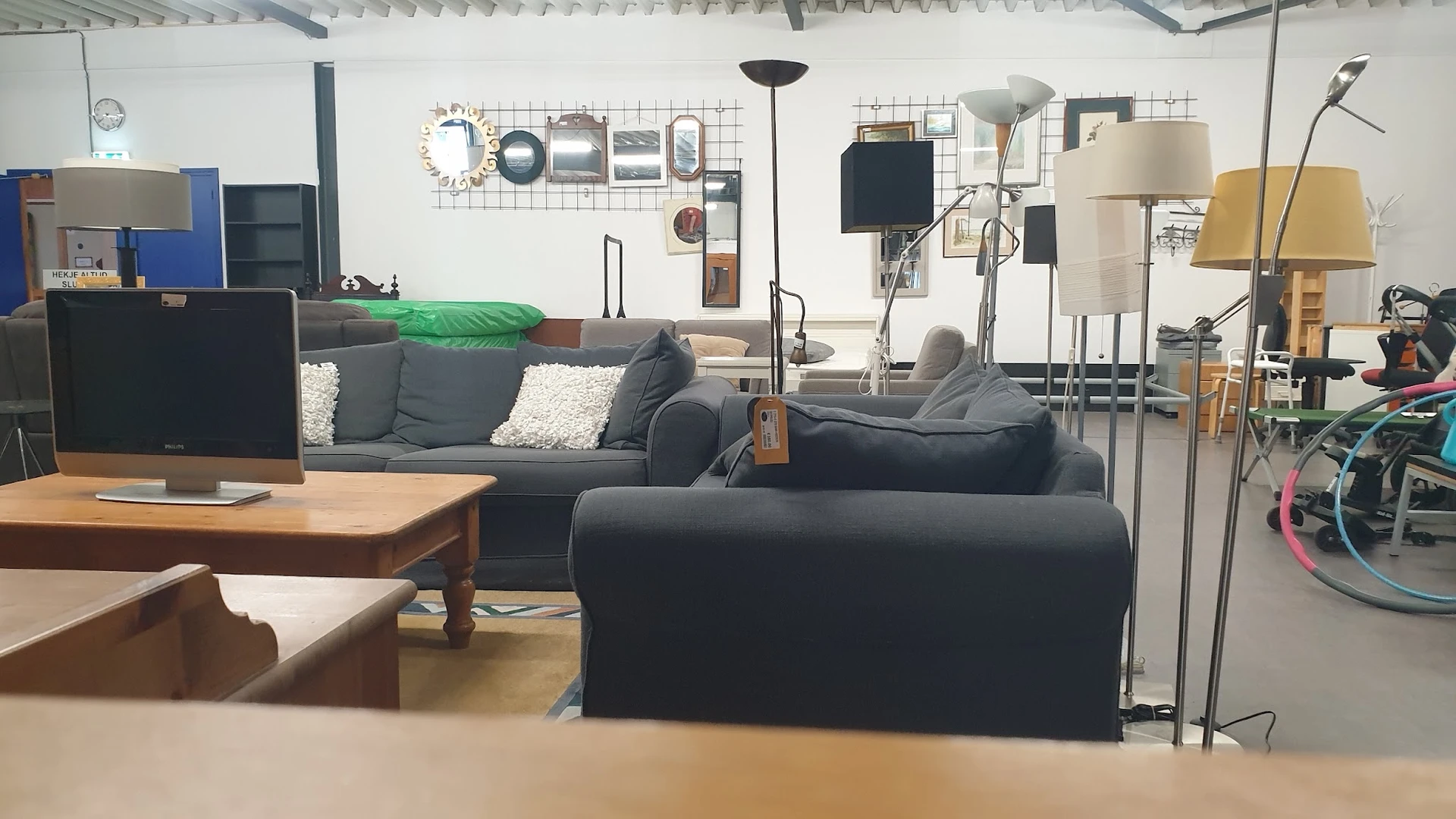 Winkelvloer met uitgestalde meubels: grijze banken, houten tafel, verschillende lampen en woondecoratie tegen de wand