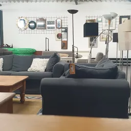 Winkelvloer met uitgestalde meubels: grijze banken, houten tafel, verschillende lampen en woondecoratie tegen de wand